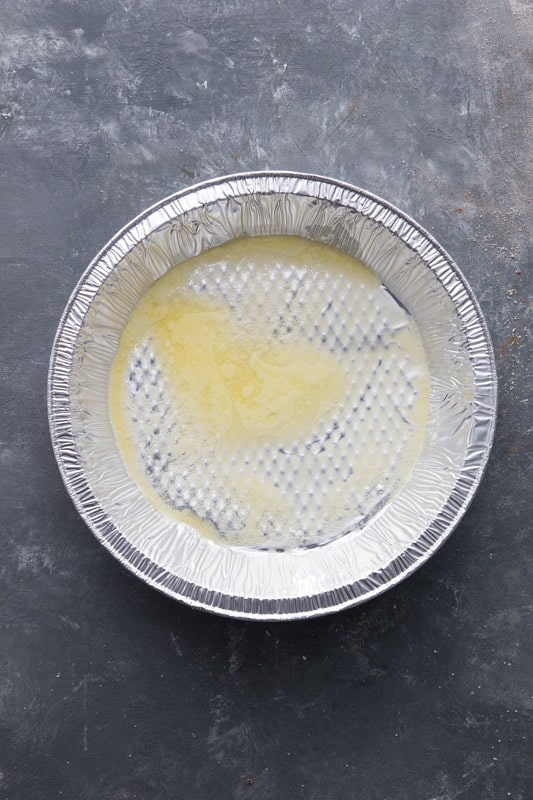 Disposable pie plate with melted butter covering the bottom