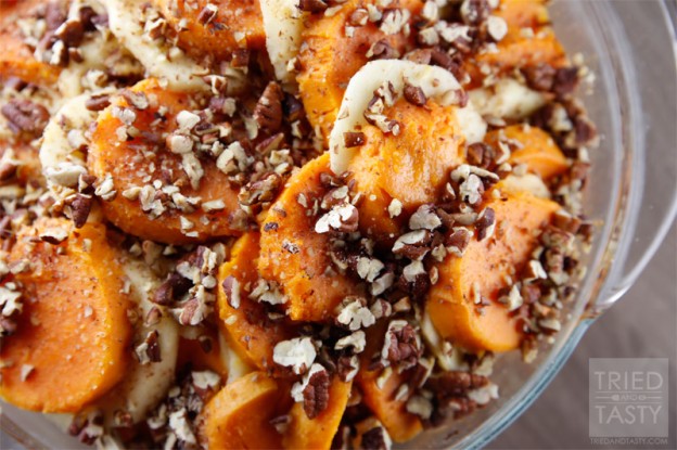 Close up shot of sliced sweet potatoes alternating with sliced apples topped with chopped toasted pecans in a glass bowl