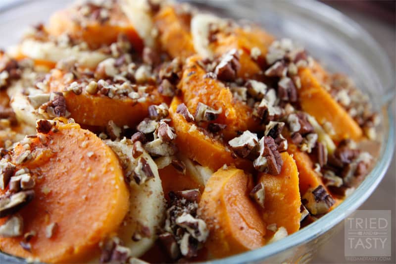 Close up image of sliced baked sweet potatoes alternating with apple slices topped with chopped toasted pecans in a baking dish