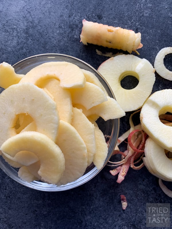 Sliced apples in a bowl with apple peel & extra slices on the counter to the right of the bowl and an apple core directly above