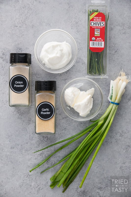 Spice jars with garlic powder, onion powder, a bowl of sour cream, a bowl of cream cheese, chives and green onions on a counter