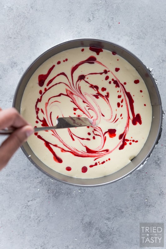 Cheesecake pan filled with batter being swirled with raspberry sauce