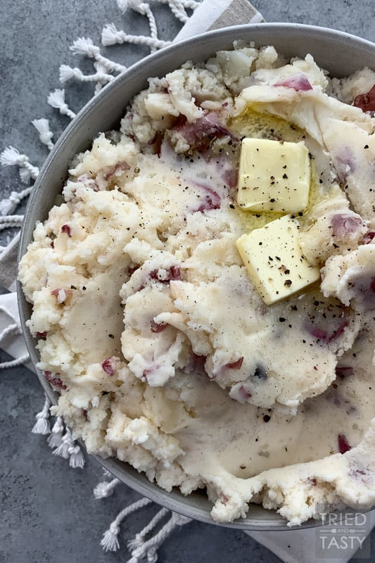 Bowl of mashed red potatoes with two squares of butter garnished with black pepper