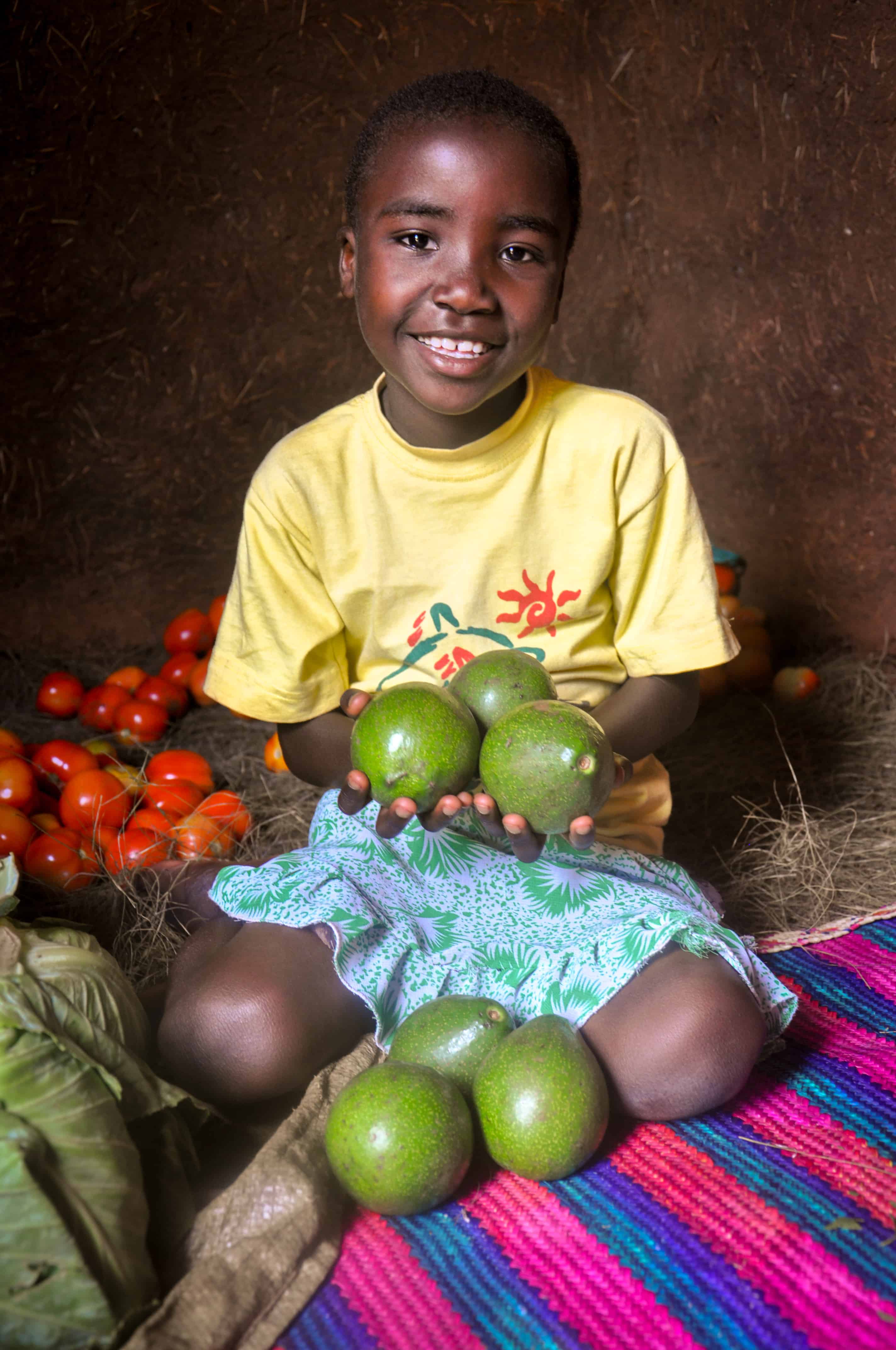 A World Vision Tanzania sponsored child Vanessa (6) happily holding avocadoes which shows food security at her home in Kitoko village located in north western Tanzania
