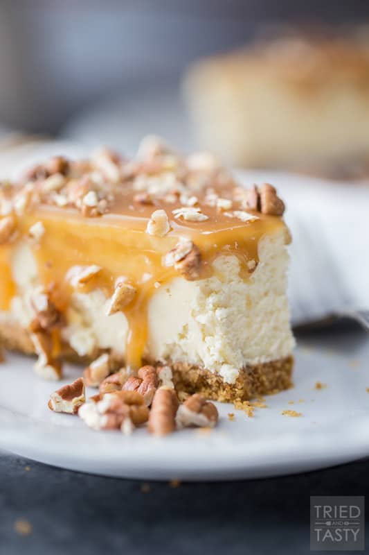 Slice of cheesecake covered in caramel & topped with pecans on a white plate with silver fork