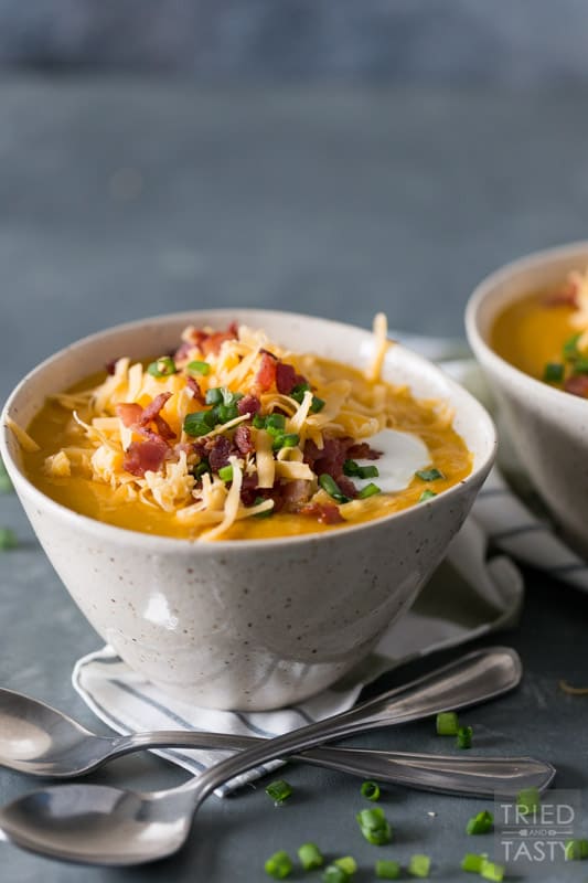 Sweet potato soup in a ceramic bowl topped with shredded cheddar, bacon, sour cream & scallions