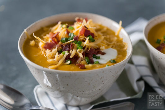Sweet potato soup in a ceramic bowl topped with shredded cheddar, bacon, sour cream & scallions