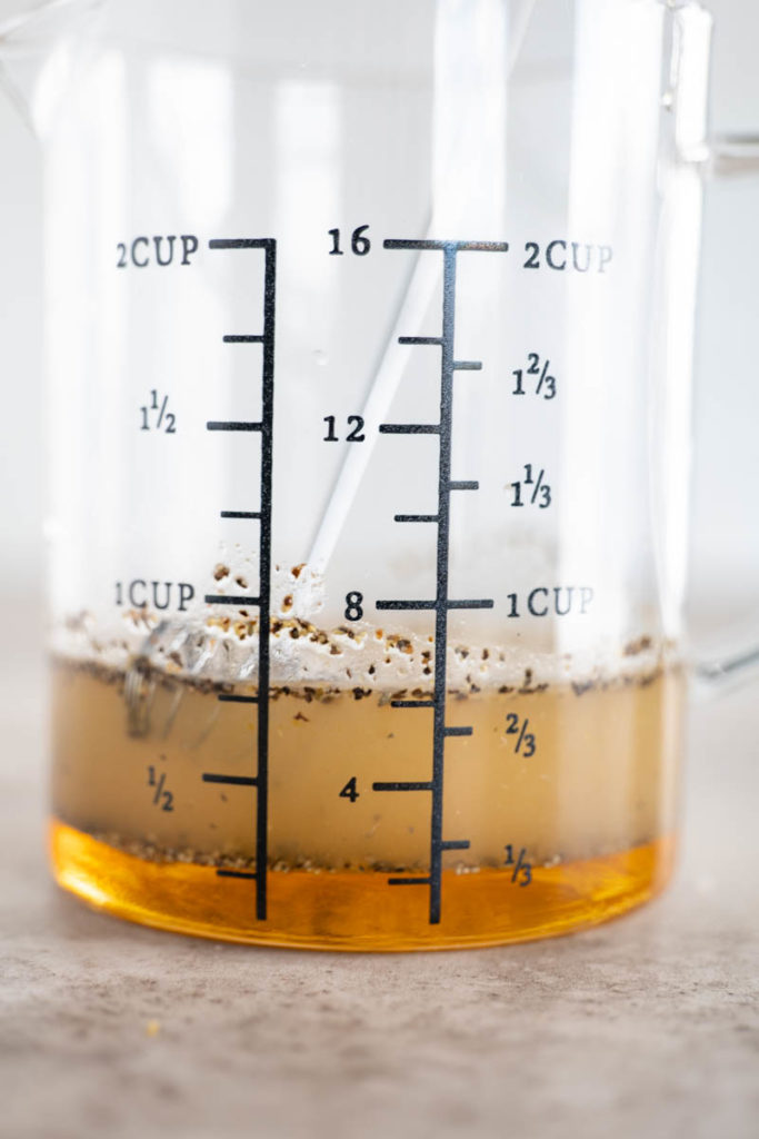 A glass measuring cup containing salad dressing with spices.